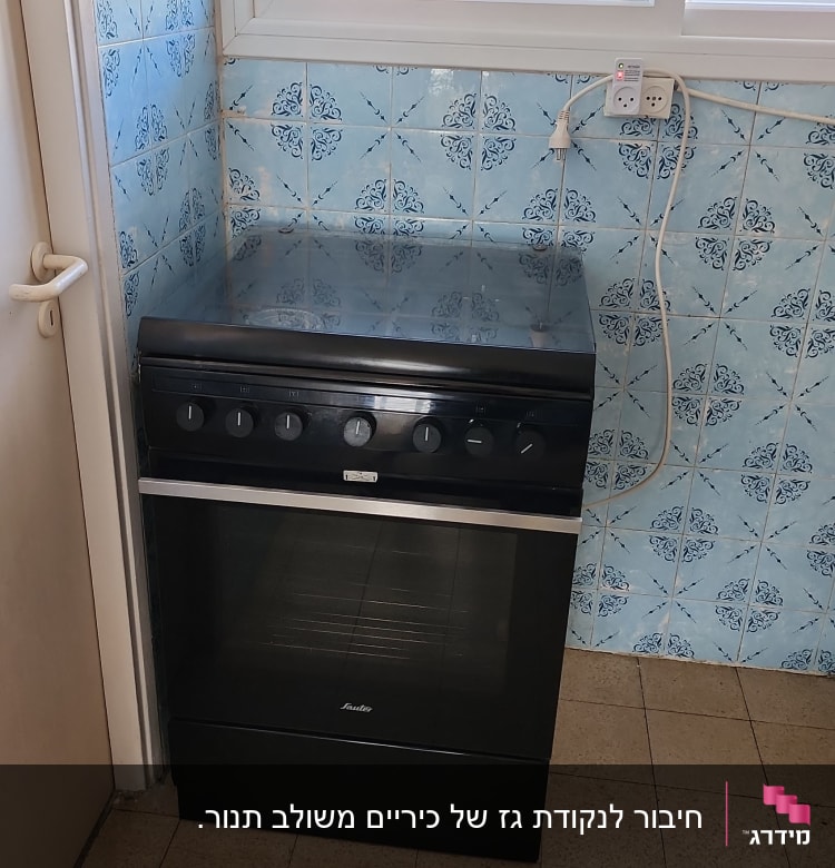 תנור שחור עם כפתורים במטבח עם אריחים כחולים